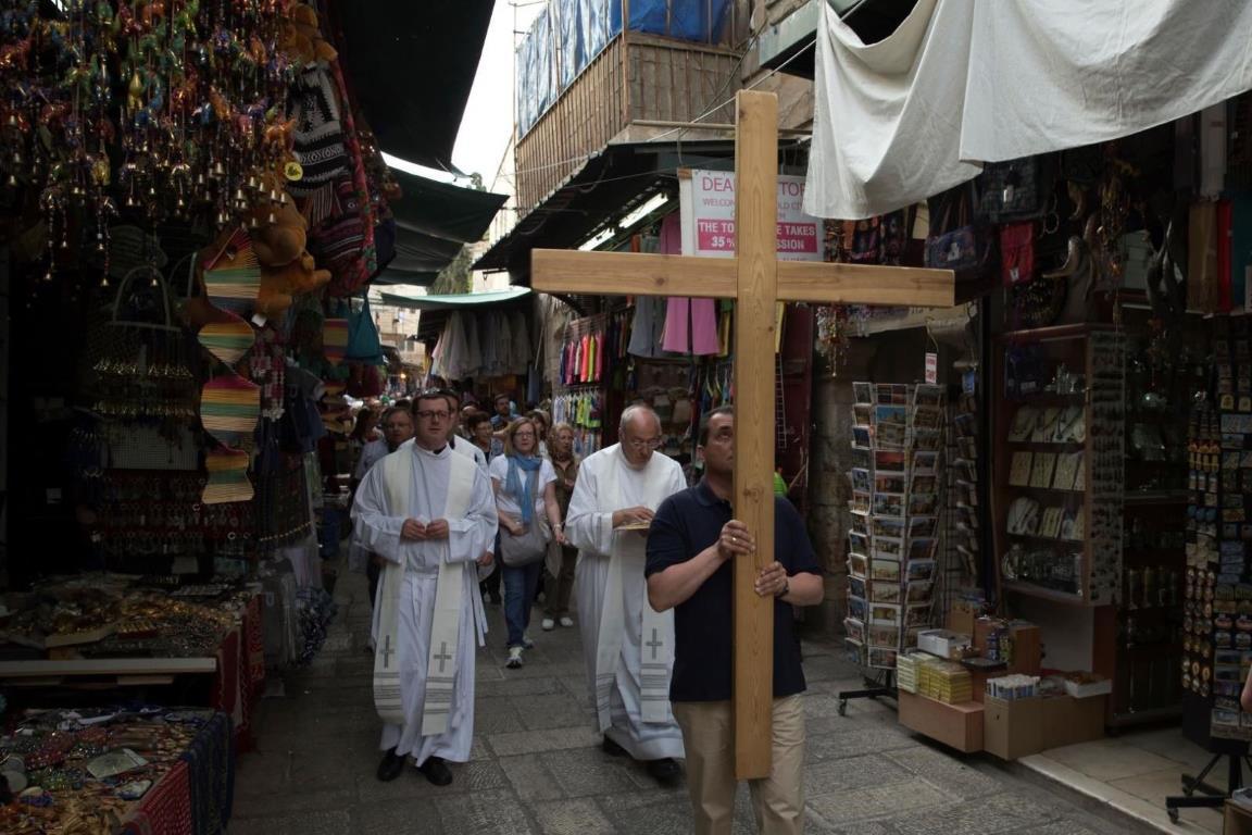 Группа католических паломников проходит мимо магазинов, продающих сувениры для туристов на Виа Долороза.