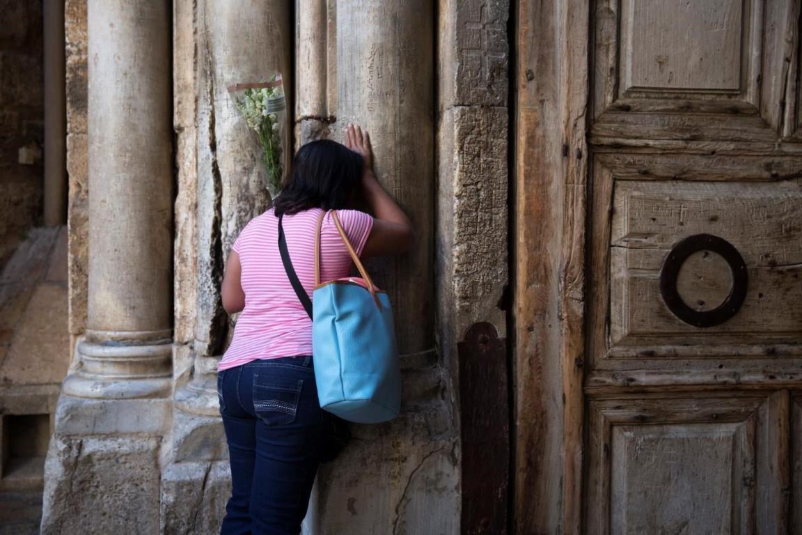 Женщина облокотилась на столб у входа в Храм Гроба Господня.