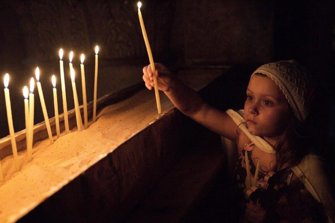 Маленькая девочка ставит свечу в Храме Гроба Господня.