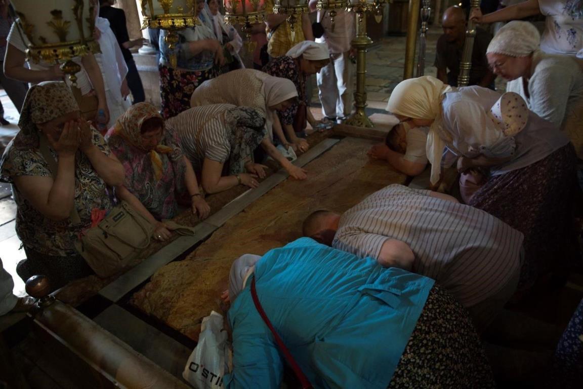 Православные паломники молятся стоя на коленях перед Камнем Миропомазания.
